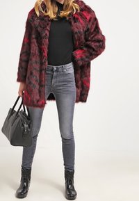 Abrigo de piel sintética con rayas rojas y negras, combinado con una blusa negra y jeans grises. Completado con botines negros brillantes y un bolso negro.