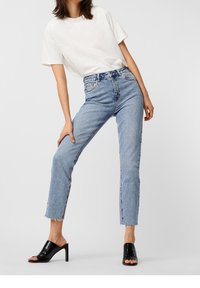 Ljusblå högmidjade jeans med fransad fåll, ihop med en enkel vit t-shirt och svarta öppna klackskor.