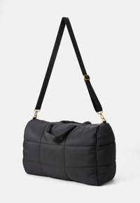Black quilted duffel bag with padded handles and adjustable shoulder strap, featuring gold-tone hardware and zipper closure.