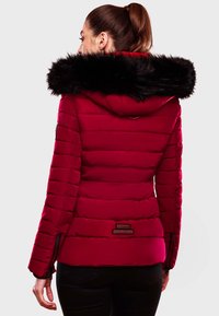 Red puffer jacket with a faux fur collar, featuring quilted texture, zippered side pockets, and branded hardware at the hem.