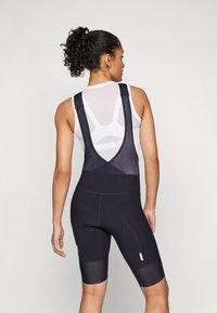 Sorte sykkel-bib-shorts med mesh-stropper, ribbet tekstur og polstret sete. Tett passform med refleksdetaljer og lengde til midten av låret.