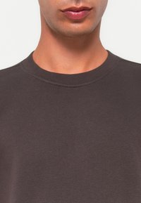 Lower face and neck of a person wearing a dark gray crewneck sweater against a plain background.