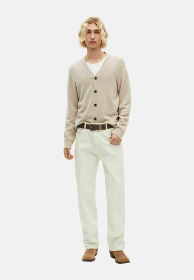 Beige cardigan met zwarte knopen, gedragen over een wit shirt, gecombineerd met witte broek en bruine schoenen, met een standaard pasvorm en een gladde textuur.