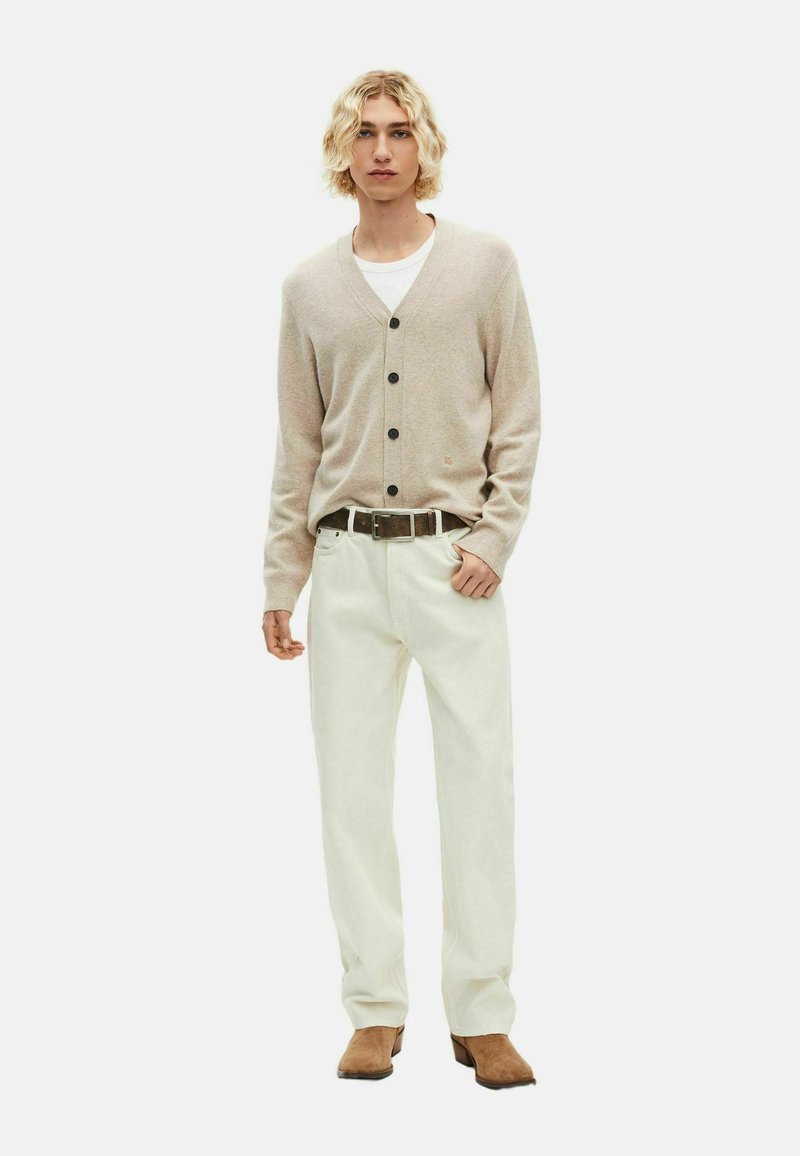 Beige cardigan met zwarte knopen, gedragen over een wit shirt, gecombineerd met witte broek en bruine schoenen, met een standaard pasvorm en een gladde textuur.