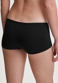 Zwarte boyshort-stijl ondergoed met een gladde textuur, elastische tailleband en minimale stiksels, bekeken vanuit de achterkant.