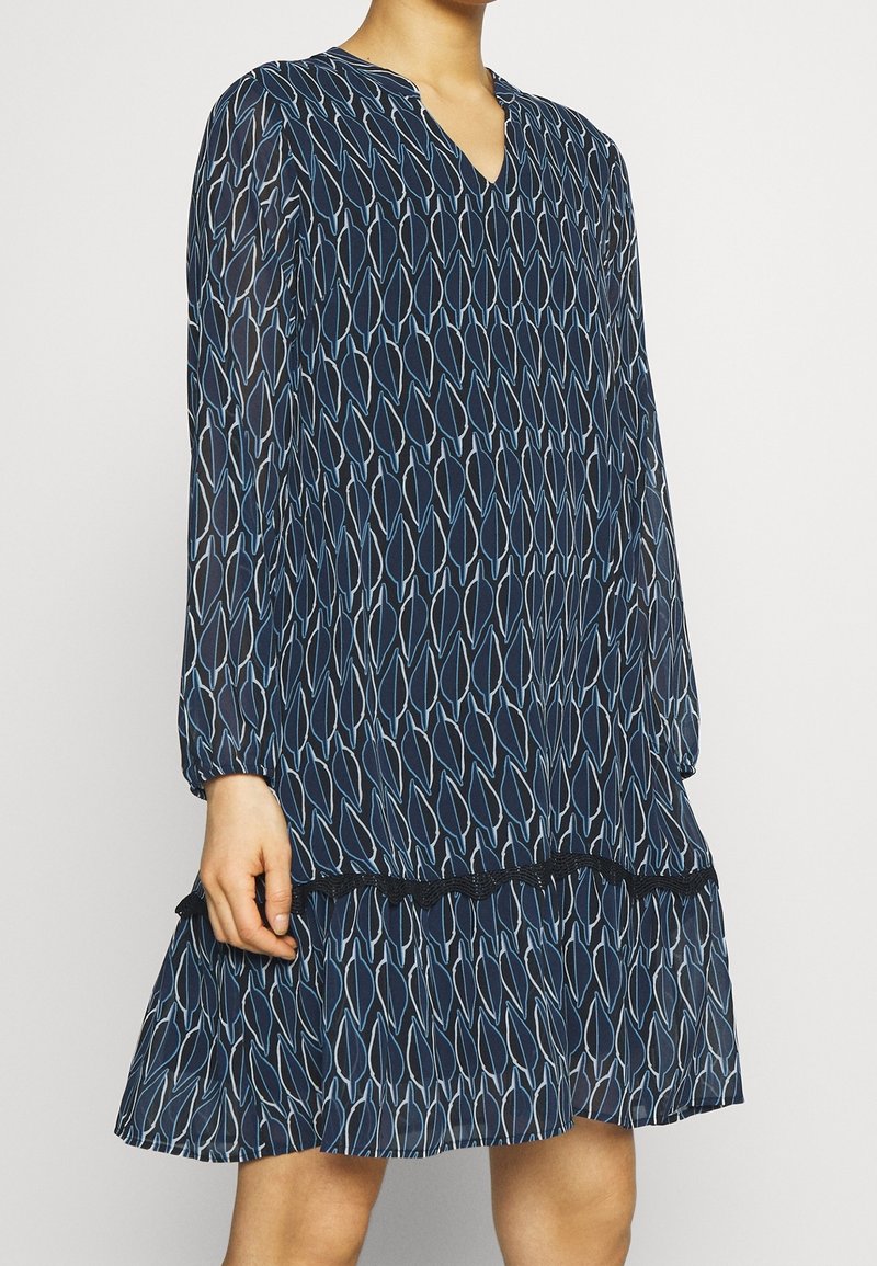 Marineblaues Kleid mit V-Ausschnitt und langen Ärmeln. Es hat ein Blattmuster in Hellblau, einen gerafften Saum und elastische Akzente an den Bündchen.