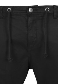 Pantalones negros con cintura ajustable con cordón, cierre de botón metálico y bolsillos delanteros. La tela parece lisa con un ligero brillo.