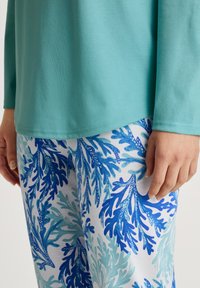 Türkises Langarmoberteil kombiniert mit weißen Hosen, die ein blaues und aquafarbenes Korallenmuster aufweisen. Baumwollstoff mit einer glatten Textur.