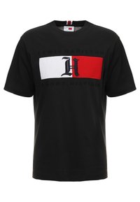 Camiseta de algodón negra con un gran gráfico en blanco y rojo que presenta un logo con la 'H'. El texto dice "Lewis Hamilton" y "Tommy Hilfiger" debajo del diseño.