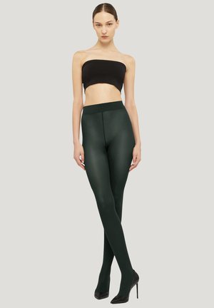 Grønne, ugennemsigtige leggings lavet af elastisk materiale, med høj talje, glat tekstur og tætsiddende pasform, kombineret med sorte højhælede sko.