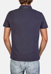 Marineblauwe polo met korte mouwen en een kraag, gemaakt van textuurstof katoen, gedragen met lichtblauwe jeans. Heeft een subtiele achterkantnaad.