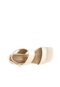 Beige korkokenkä korkean kantapään kanssa, jossa on leveät päälliset ja nilkkahihna. Neliömäinen kärki, jossa on sileä nahkatekstuuri ja neutraali väri.