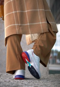 Vita atletiska sneakers med flerfärgade accenter i rött, blått och teal, med texturerade svarta gummisulor och snörningsdesign.