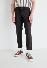 Temno rjave krojene hlače slim fit, z naborki, stranskimi žepki in v kombinaciji z rjavimi in belimi supergami.