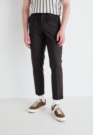 Dark brown tailored trousers with a slim fit, featuring pleats, side pockets, and paired with brown and white sneakers.