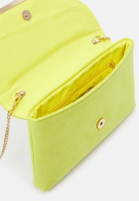 Pochette en daim vert avec une fermeture à clip dorée. Comprend une poche intérieure zippée et une bandoulière chaîne amovible dorée. Ouverte pour montrer l'intérieur.