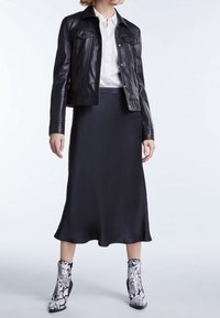 Giacca di pelle nera sopra una blusa bianca, abbinata a una gonna di raso nera e stivaletti stampati con motivo serpente.