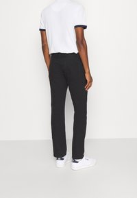 Musta slim fit -farkut, joissa on takataskut, yhdistettynä valkoiseen t-paitaan, jossa on laivastonsiniset reunukset, ja valkoisiin lenkkareihin.