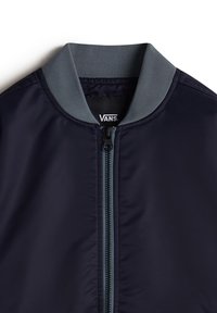 Blouson aviateur bleu marine avec col côtelé gris et fermeture éclair, portant une étiquette de la marque Vans à l'intérieur du col.