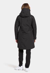 Parka nera impermeabile con cappuccio, dotata di vita cintrata, maniche lunghe e due tasche laterali. Texture liscia, design di lunghezza media.