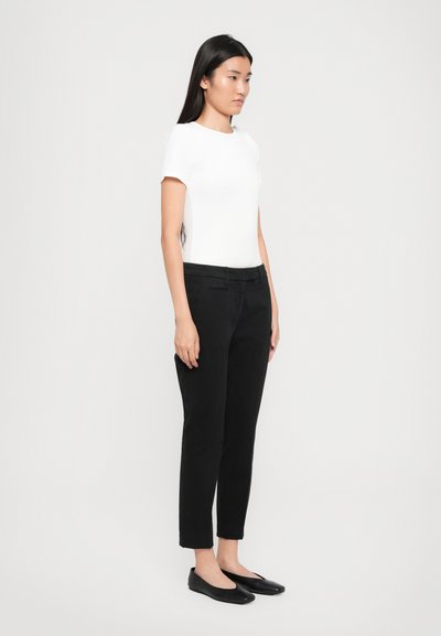 T-shirt blanc à manches courtes associé à un pantalon noir fuselé et des ballerines noires. Design simple, texture lisse et silhouette ajustée.