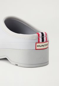 Biele gumové dreváky so šedou podrážkou, s červeným, čiernym a bielym pruhovaným akcentom vzadu a logom "HUNTER".