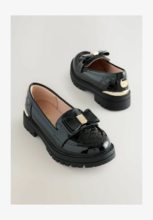 Fekete lakk loaferek textúrált felsőrésszel, nagy masni díszítéssel és arany hardware-rel. A robusztus fekete talp magasságot és stabilitást ad.