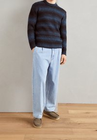 Maglione a righe blu navy in maglia con scollatura a coste, abbinato a jeans baggy azzurri e scarpe slip-on marroni su un pavimento di legno.