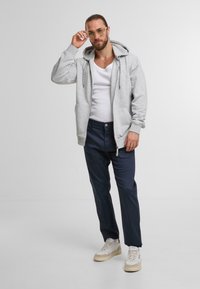 Jasnoszara bluza z zamkiem, z przednimi kieszeniami, w połączeniu z granatowymi spodniami i białymi trampkami. Minimalistyczny design, miękka tkanina i luźny krój.