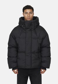 Giacca a vento nera con colletto alto e grande cappuccio, caratterizzata da un design trapuntato e tasche laterali, realizzata in materiale liscio e leggero.