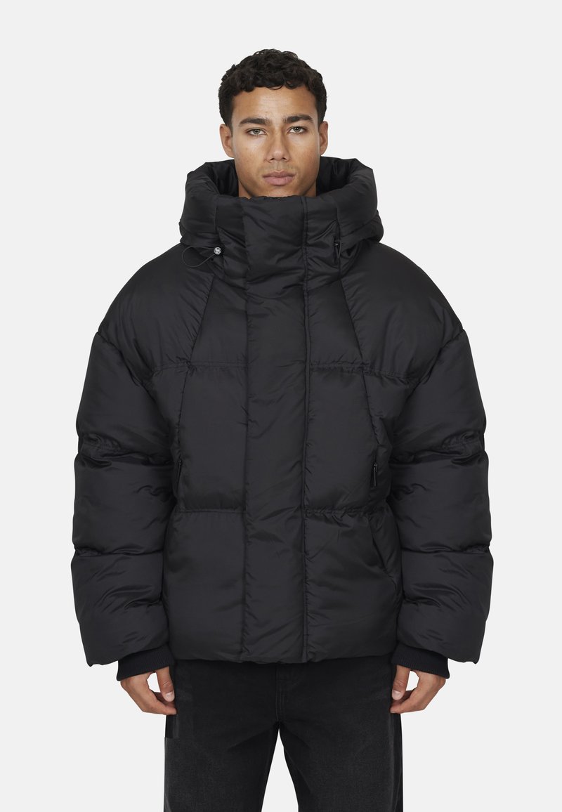 Giacca a vento nera con colletto alto e grande cappuccio, caratterizzata da un design trapuntato e tasche laterali, realizzata in materiale liscio e leggero.