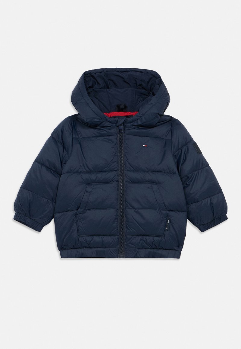 Mornarsko modra prešita jakna za dojenčke s kapuco, sprednjim zadrgo, dvema žepoma, elastičnimi manšetami in majhnim logotipom blagovne znamke na prsih in rokavu.