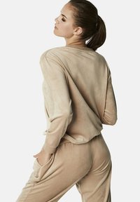 Beige velours loungewear set met een relaxte pasvorm, voorzien van een long-sleeve top met ribgebreide manchetten en bijpassende broek met zijzakken. Gladde textuur.