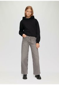 Sweat-shirt à capuche noir avec poche avant, pantalon en jean large gris, bottines noires, posture droite, fond clair.