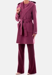 Cappotto lungo, con cappuccio, di lana rosa intenso con cintura e due tasche frontali, abbinato a pantaloni a palazzo coordinati. Tessuto morbido e vestibilità comoda.