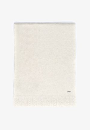 Biały dziergany koc z fakturowanym wzorem warkocza wzdłuż dolnej krawędzi, z małą, dyskretną metką marki w jednym rogu.