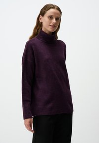 Gebreide turtleneck trui in diep paars met geribde kraag en manchetten. Ontspannen pasvorm, zachte textuur en ontwerp tot op de heup.