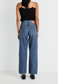 Breda ben blå denimjeans med hög midja, femfickorsdesign och synlig sömnad. Har en läderlogotyp på baksidan.