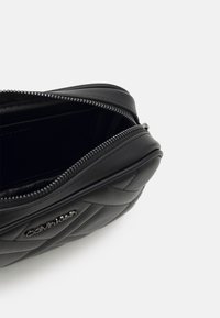 Czarna pikowana skórzana torba z zamkiem błyskawicznym, ozdobiona srebrnym logo. Okrągły kształt o gładkiej fakturze i metalowe okucia zamka.