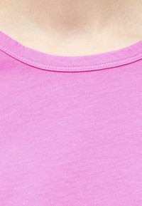 Gros plan sur la partie supérieure de la poitrine et le cou d'une personne portant un t-shirt rose uni à col rond.