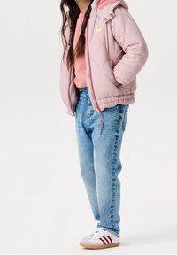 Veste matelassée rose clair, sweat-shirt rose, jean bleu clair et baskets blanches avec des accents rouges. Textures lisses, coupe décontractée.