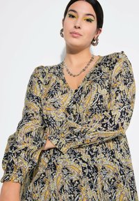Robe à manches longues avec un décolleté en V, en tissu noir orné de motifs paisley jaunes et blancs, avec des détails de manches froncées.