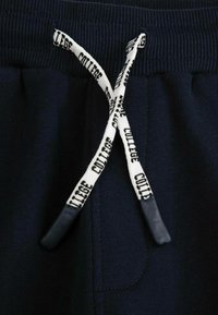 Granatowe dresowe spodnie z białym sznureczkiem, na którym znajduje się czarny napis "LICE COLLEGE", związanym luźno węzłem w talii.