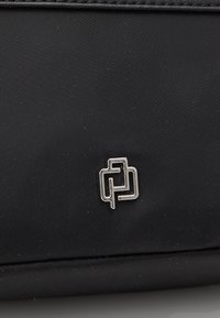 Czarna torba z tkaniny z srebrnym geometrycznym logo. Powierzchnia ma gładką teksturę z subtelnymi detalami szwów.