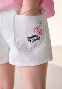 Shorts in denim bianco con tasca posteriore decorata da un ricamo raffigurante due ciliegie rosa sorridenti e la scritta "Smiley World".