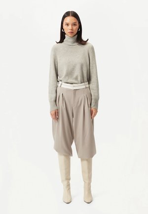 Pull en col roulé gris, pantalons beiges plissés et bottes beiges jusqu'aux genoux. Textures lisses, coupe ajustée et détail de ceinture contrastante.