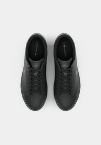 Μαύρα δερμάτινα αθλητικά παπούτσια με στρογγυλές μύτες, επίπεδα κορδόνια και ελαστικές σόλες. Περιέχουν το λογότυπο Lacoste σε πράσινο στη πλευρά και έχουν υφή.