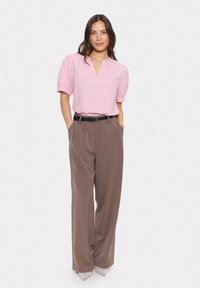 Rosa Bluse mit kurzen Ärmeln und V-Ausschnitt, kombiniert mit hoch taillierten, weit geschnittenen braunen Hosen und glänzenden spitzen Absätzen.