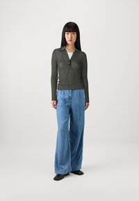 Dunkelgraues, geripptes Langarmoberteil mit kragenförmigem Ausschnitt und Knopfdetail, kombiniert mit hellblauen weit geschnittenen Jeans und schwarzen flachen Schuhen.
