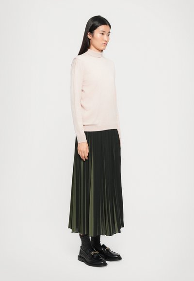 Light pink turtleneck sweater, paired with a pleated dark green skirt. Model wears black loafers and gray socks. Minimalist design and textures.